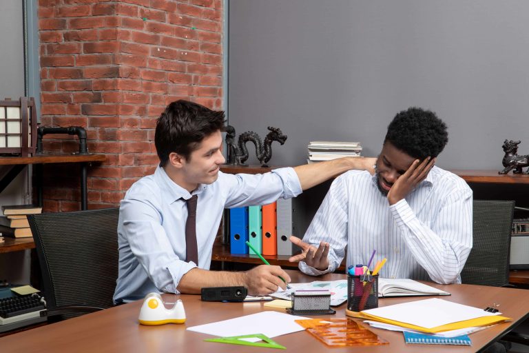 Two businessmen discuss a project, one placing a hand on the other’s shoulder in a supportive gesture.