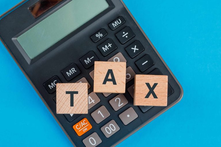 Flat lay of wooden cubes and calculator on a blue table representing tax planning for GST return preparation.